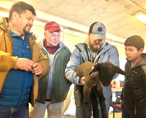 Three men, a boy and a lamb Three men and a young boy, the one on the second to the right is holding a black lamb as the boy on the far right and the others look on.