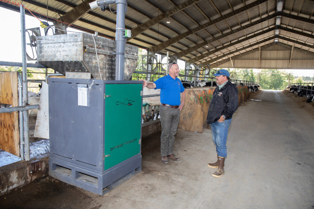 Two people talking in a dairy barn next to a feed dispenser