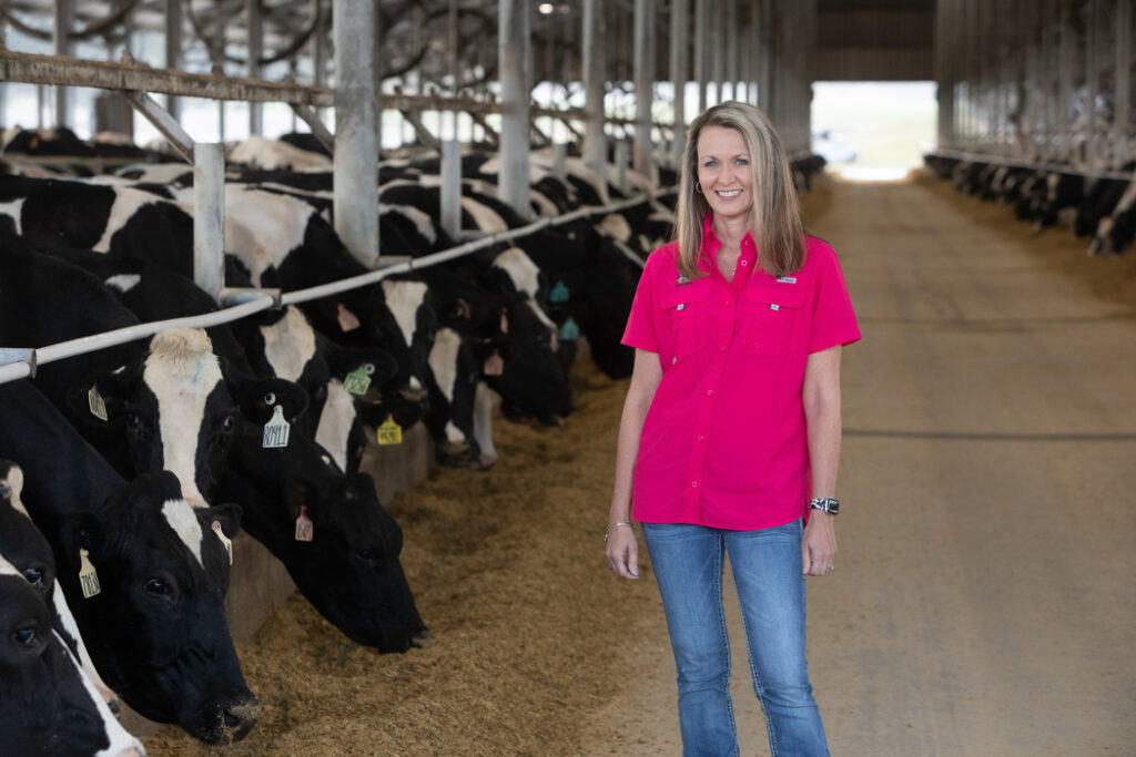 Smiling person in dairy barn next to row of cows