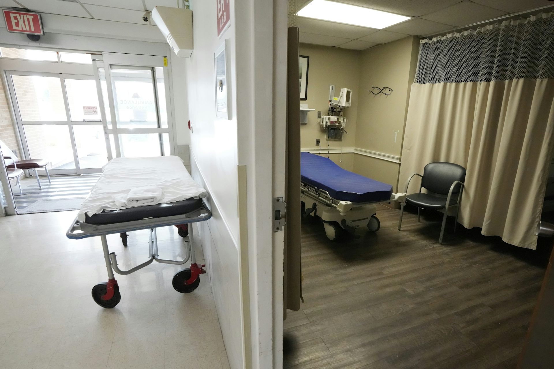 Two empty hospital beds in a room and a hallway near the entrance