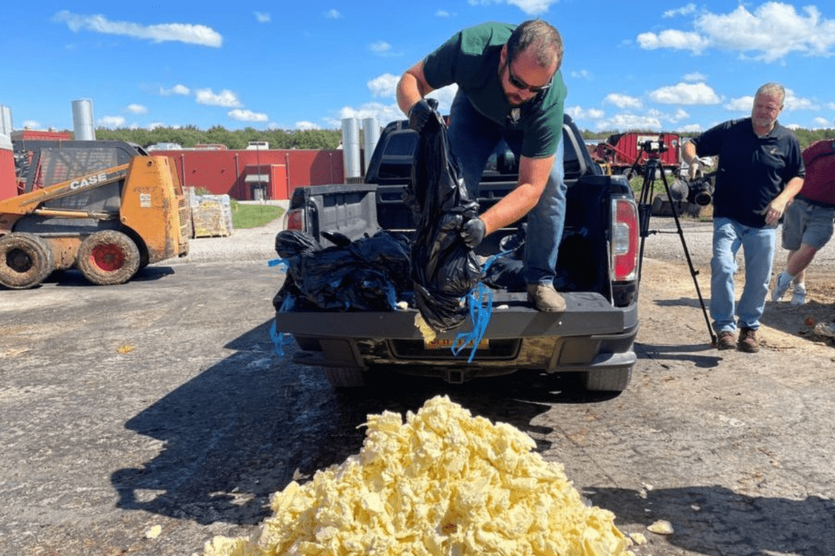 A man on a truck emptying a large black bag filled with butter on the ground.