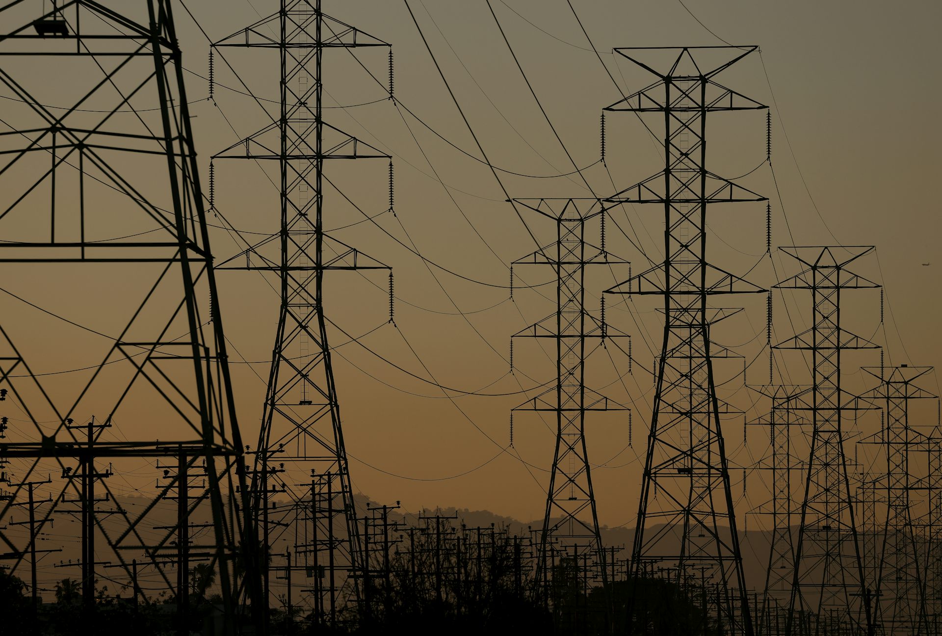 Rows of transmission towers and power lines silhouetted against a hazy sky